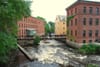 A river running through a town with ivy-covered buildings and trees on both sides. A footbridge crosses the river.